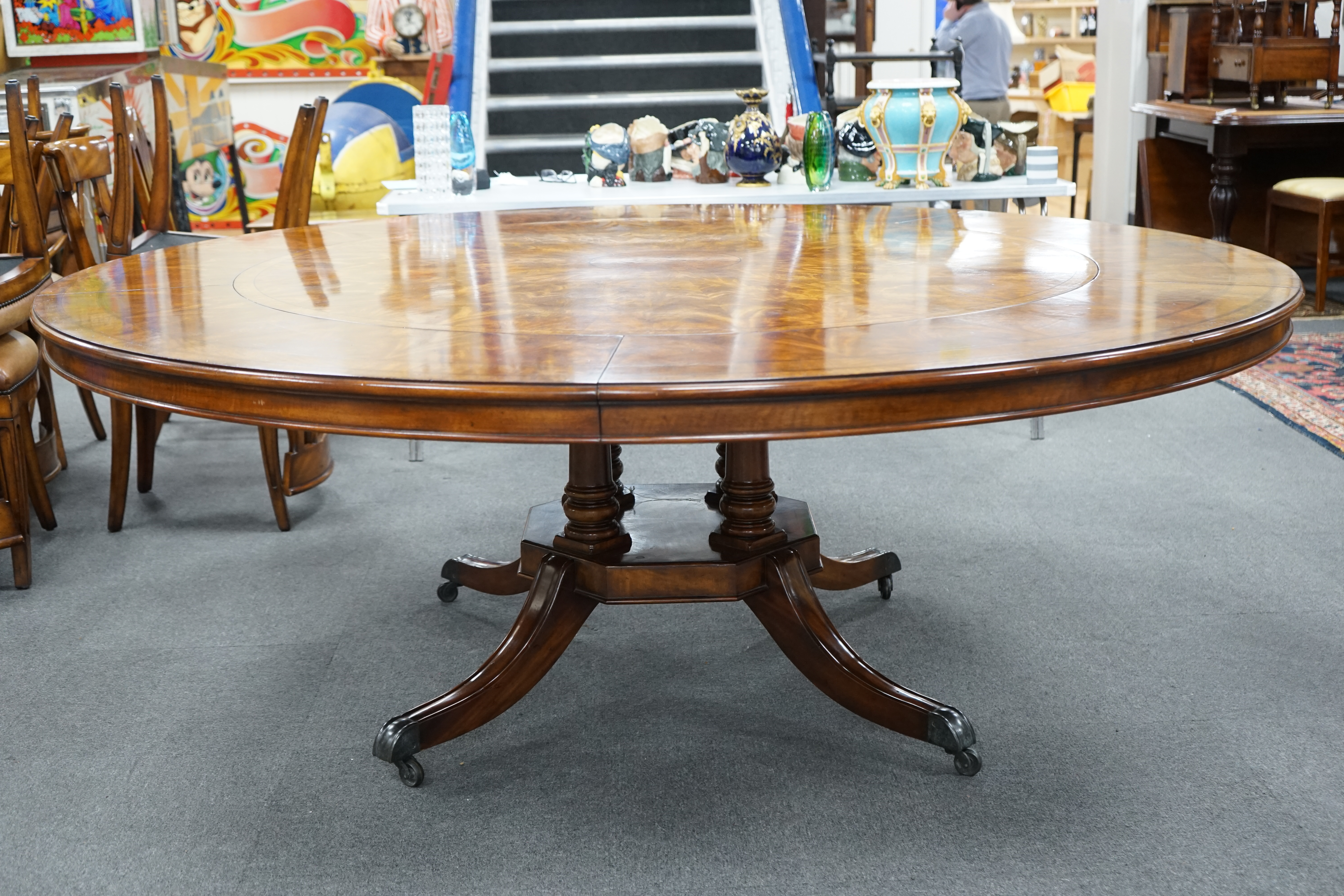 A reproduction George III style circular mahogany extending dining table with detachable segmental outer ring and eight Empire style cherry dining chairs with tan leather seats, table 142cm diameter, 202cm diameter exten